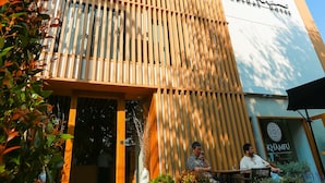 Een modern gebouw met een verticale houten gevel, een heldere lucht en terrasstoelen met plantenpotten.