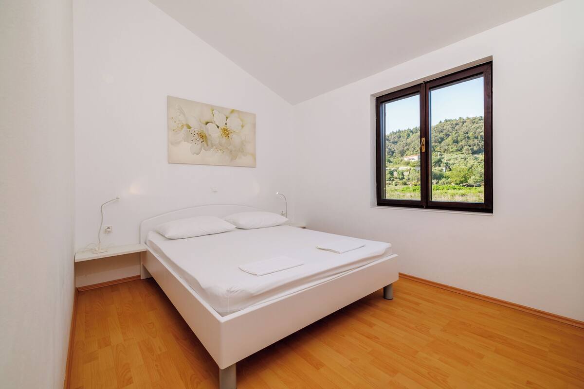 Un dormitorio con cama, ventana con vistas y un cuadro en la pared.
