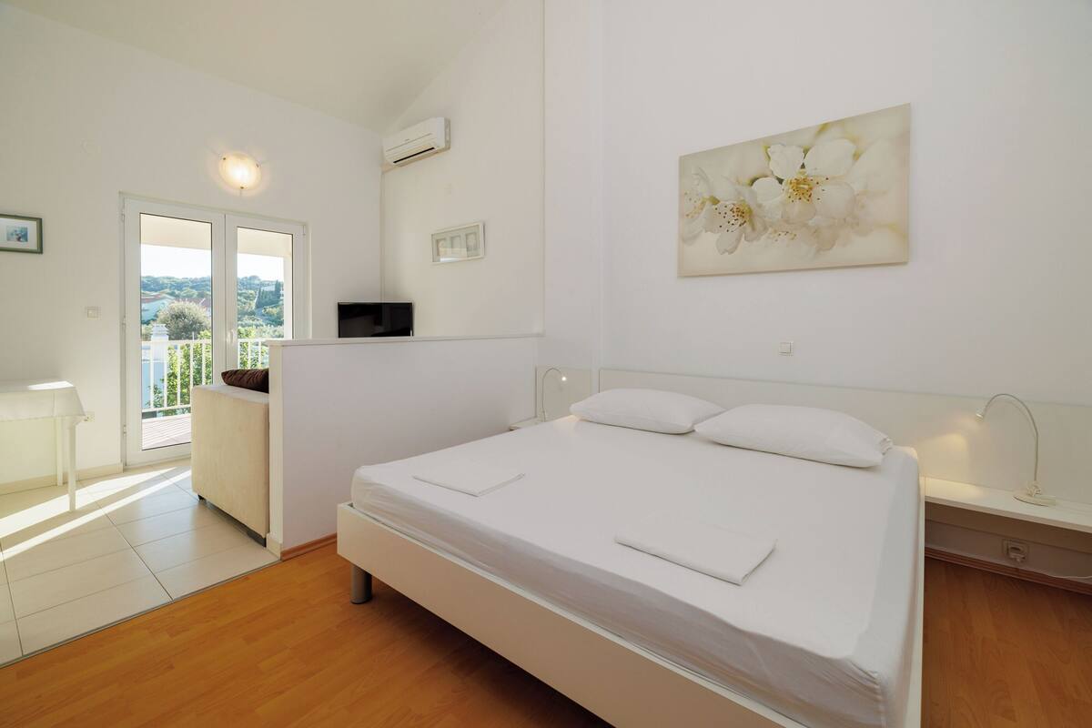 Un dormitorio con una cama grande, una mesita de noche, una silla, un televisor y vistas al exterior.