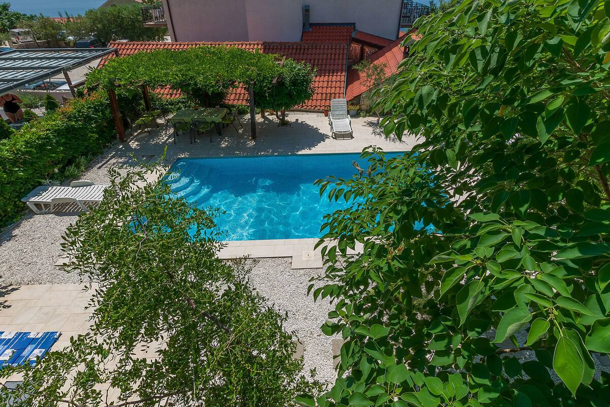 A swimming pool with lounge chairs, surrounded by trees and a tiled roof.