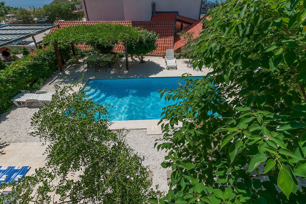 A swimming pool with lounge chairs, surrounded by trees and a tiled roof.
