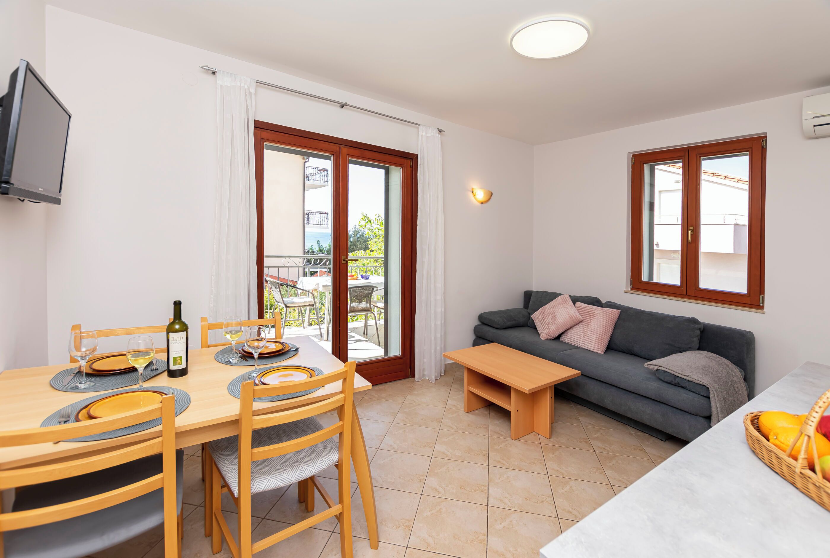 Un coin repas avec une table dressée pour deux personnes, un canapé et un petit banc en bois.