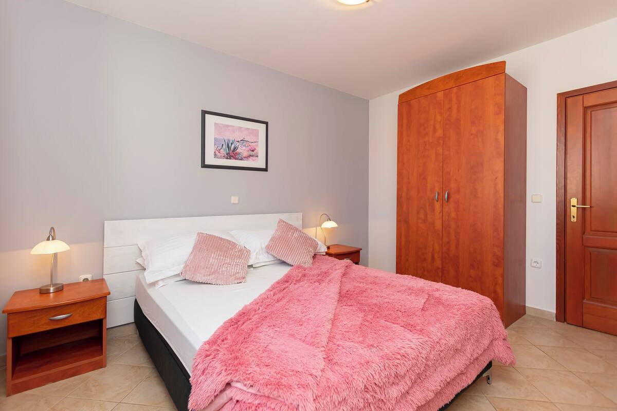 A bedroom with a bed, nightstands, a wooden wardrobe, and a framed picture on the wall.