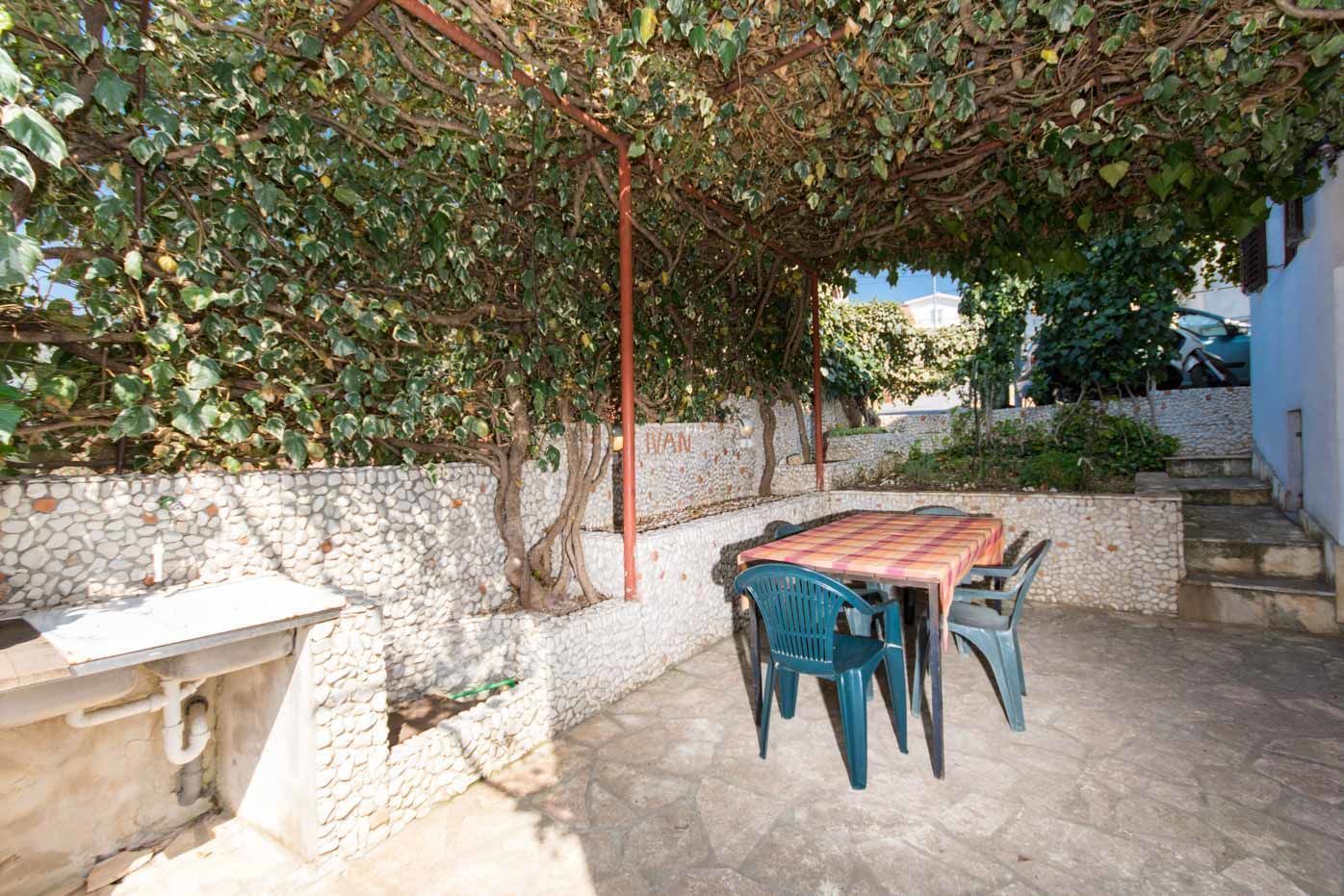 Eine Terrasse im Freien mit Tisch und Stühlen, einer Steinmauer und einer mit Wein bewachsenen Pergola.