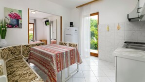 Una habitación compacta con una mesa de comedor, un sofá, un área de cocina y vistas a la vegetación por una ventana.