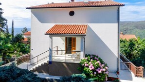 Una casa de dos pisos con techo de tejas, una escalera que conduce a la entrada y un pequeño porche.