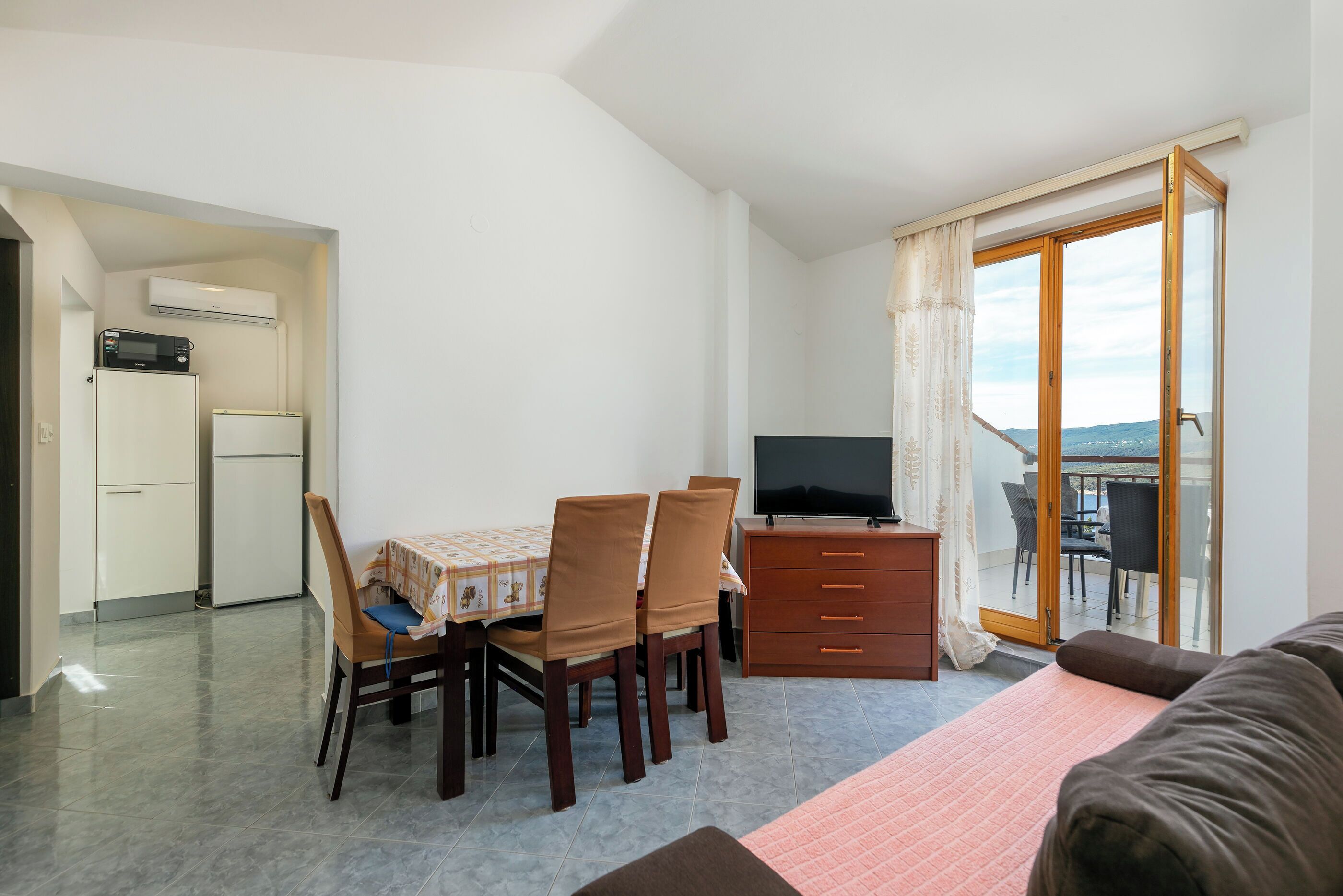 Une pièce compacte comprenant une table à manger, des chaises, un téléviseur, un canapé, un balcon avec vue et une kitchenette.