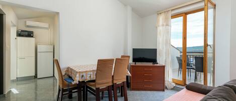 Une pièce compacte comprenant une table à manger, des chaises, un téléviseur, un canapé, un balcon avec vue et une kitchenette.