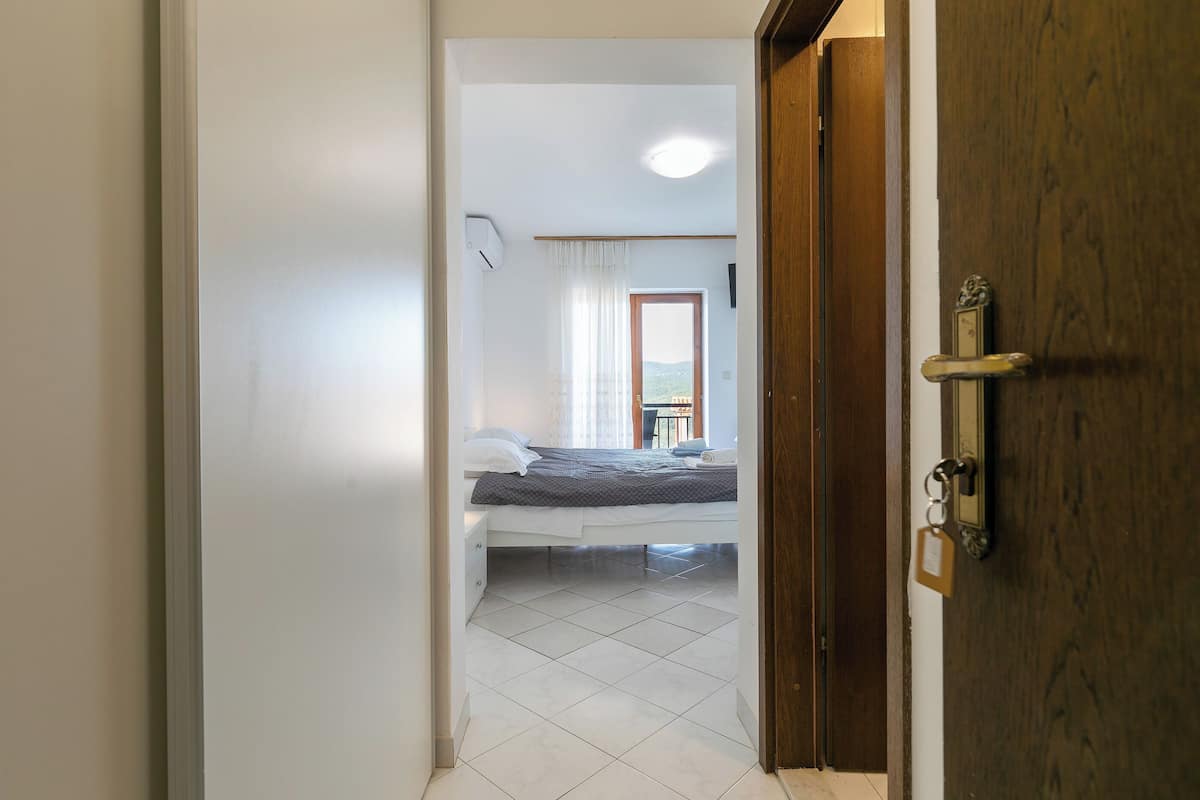 A bedroom with a bed, a bedside table, a window with curtains, and a door with a keyhole.
