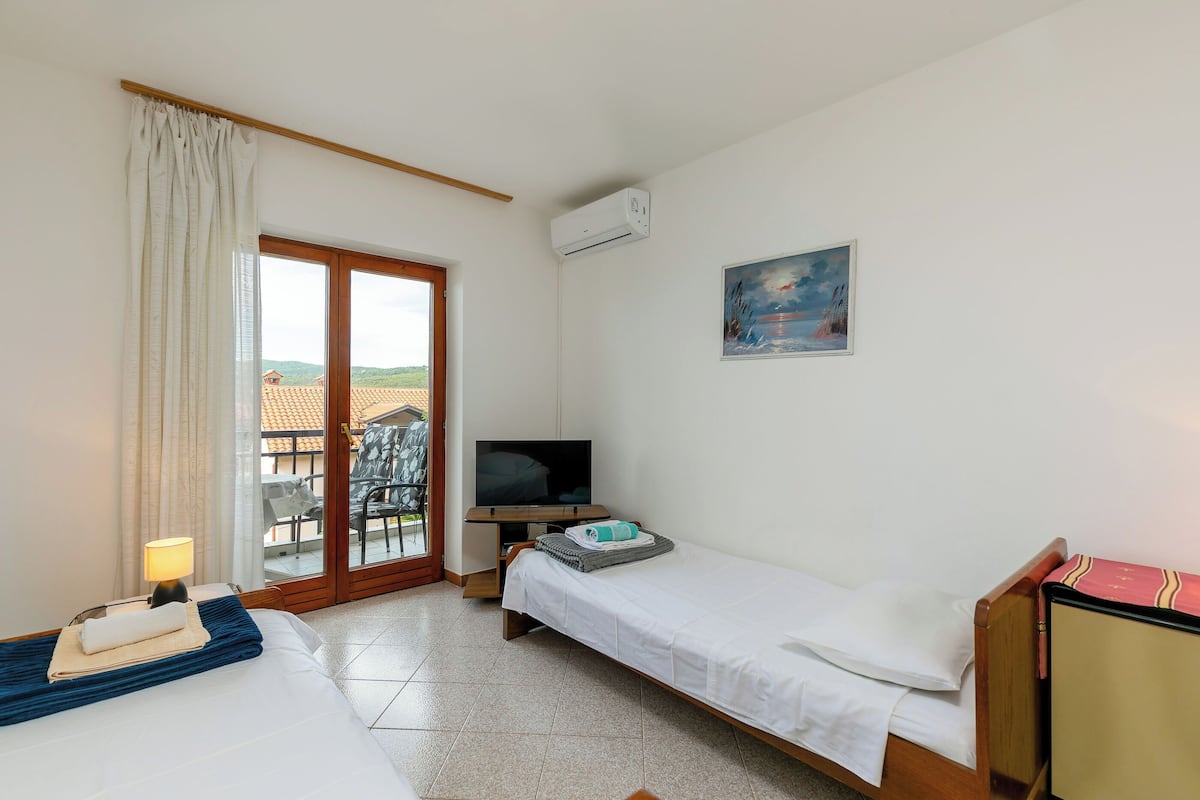 A hotel room with two beds, a TV, a painting, and a balcony with a view.