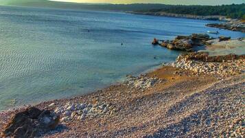 A pebbled beach with calm water, boats, and rocky outcrops.