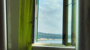 Una ventana con vista a una playa y colinas boscosas.