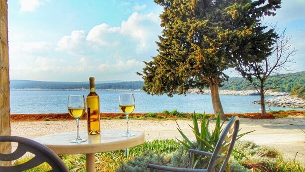 Una mesa con una botella y dos copas de vino, una silla y vistas al mar y las colinas.