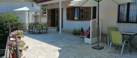 An outdoor patio area with stone flooring, green chairs, white umbrellas, and potted plants.