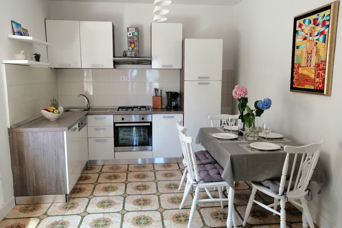 Une cuisine compacte avec des meubles blancs, un four encastré et un coin repas avec une table dressée pour deux personnes.