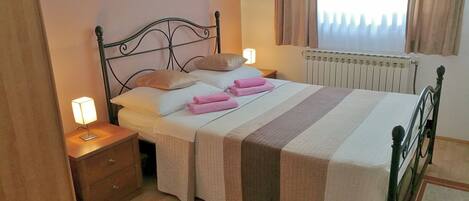 A neatly made bed with pink towels, a bedside lamp, and a radiator.