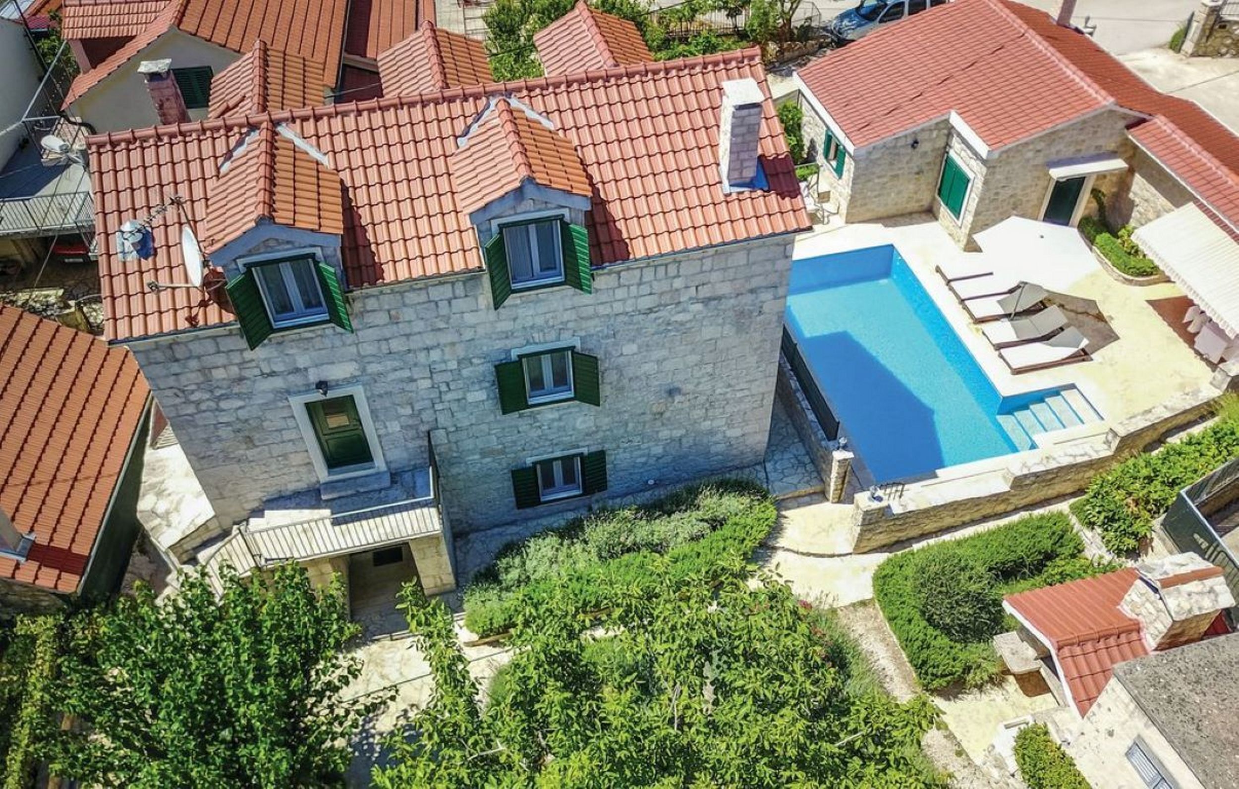 Un bâtiment en pierre doté d’une piscine, de nombreuses fenêtres et d’un toit recouvert de tuiles rouges.