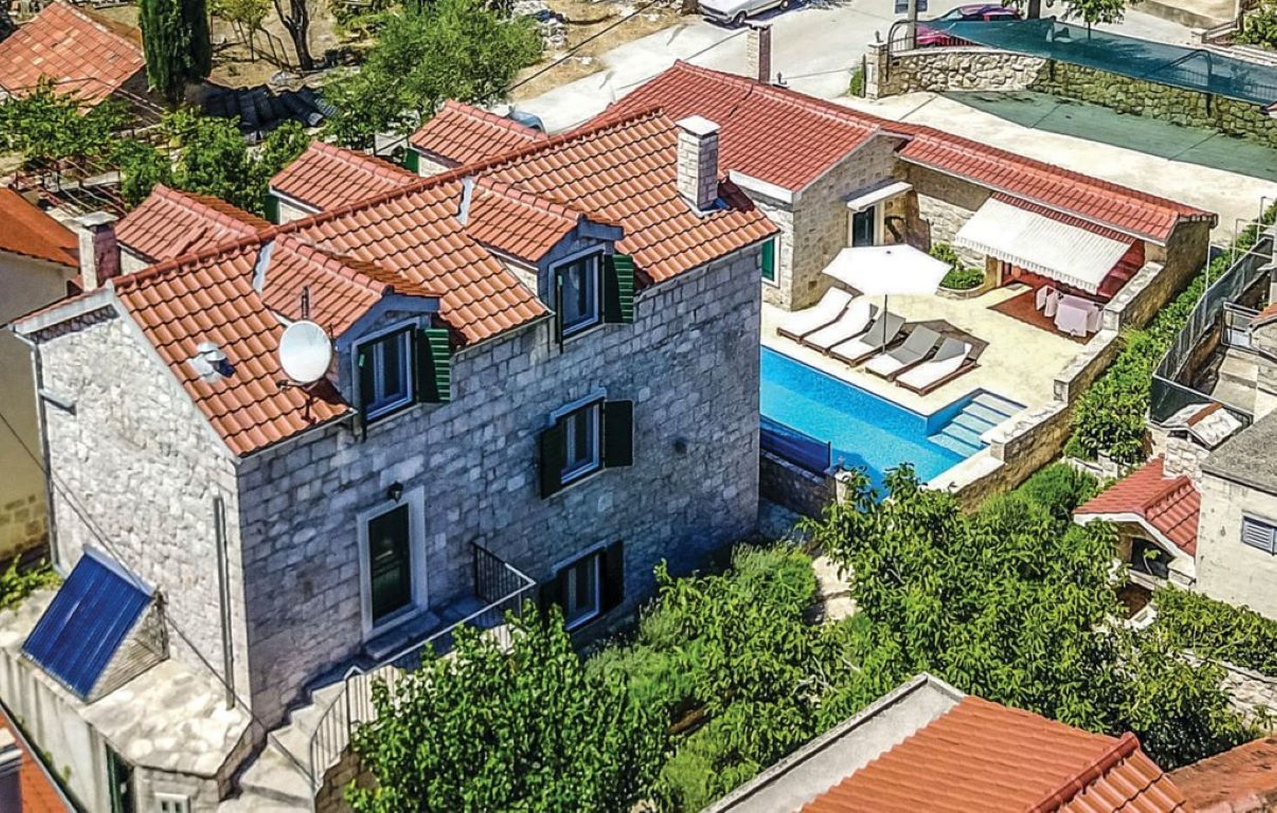 Un edificio de piedra con techo de tejas rojas, piscina y un pequeño patio.