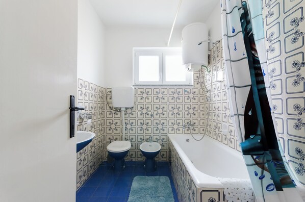 A bathroom with a bathtub, two toilets, and a window. - Apartment Josip (Senj)
