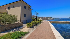A coastal building with a paved walkway leading to a body of water, stone walls, and greenery. - Apartments Darko by the sea (Supetarska Draga)