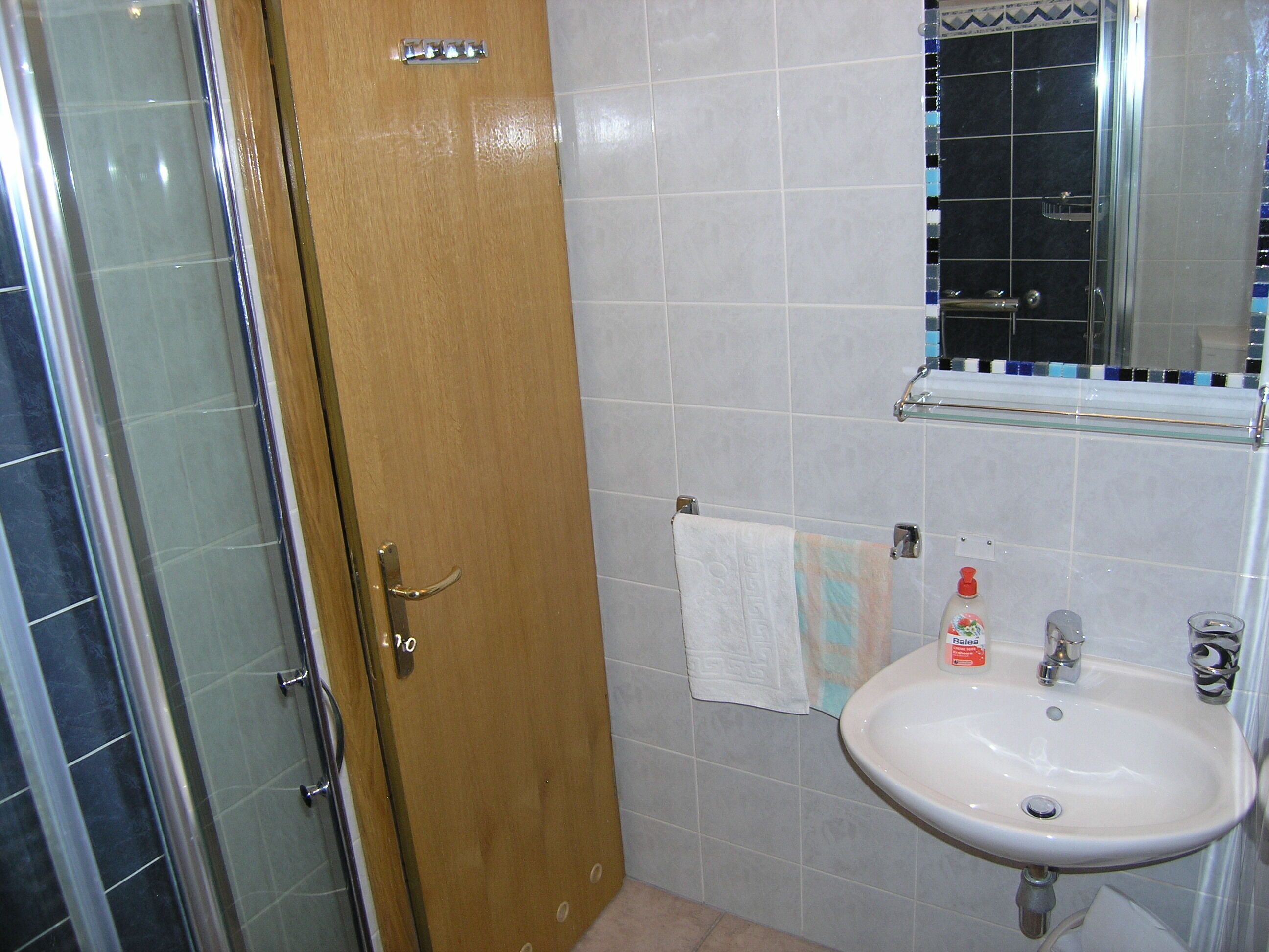 A bathroom with a wooden door, a white sink, a mirror, and a tiled wall.