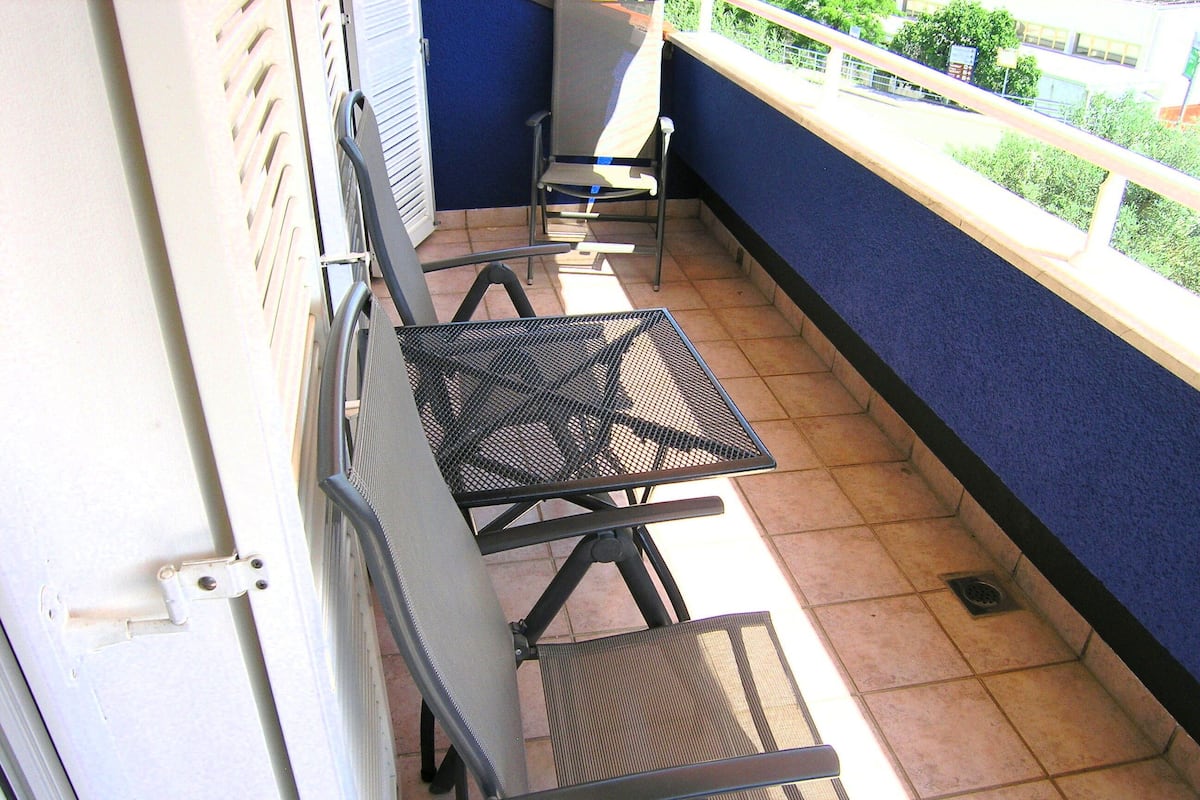 A balcony with four metal tables and chairs, a blue wall, and a view of greenery.
