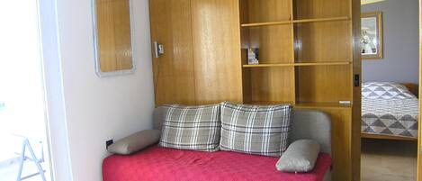 A bedroom with a bed, a wardrobe, a mirror, and a door leading to another room.