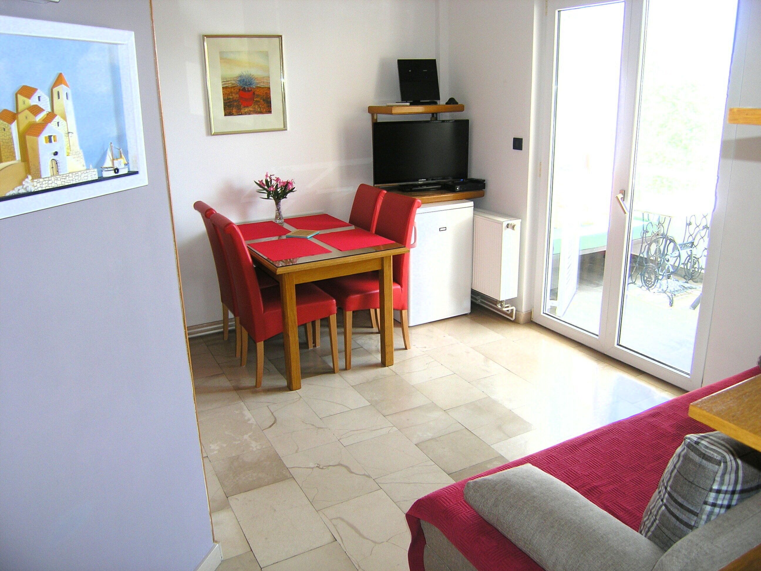 A compact room with a dining table, chairs, a small refrigerator, and a television.