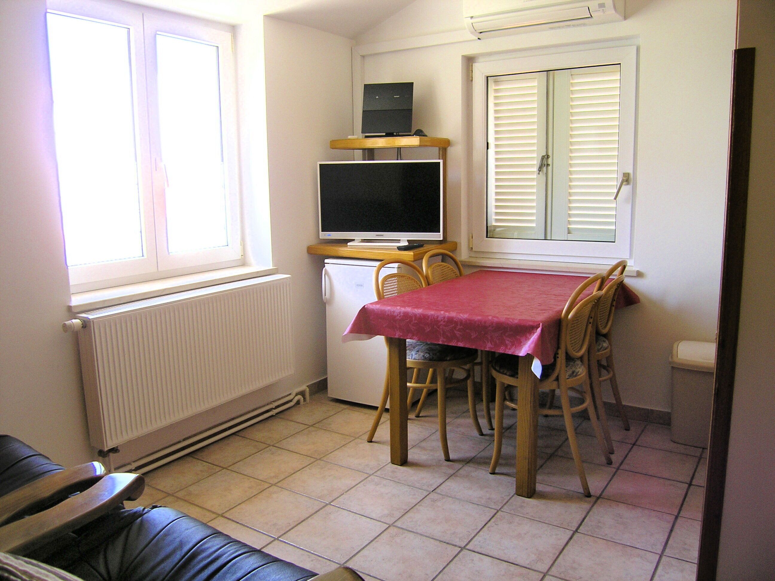 A compact room with a dining table, chairs, a television, and a small refrigerator.