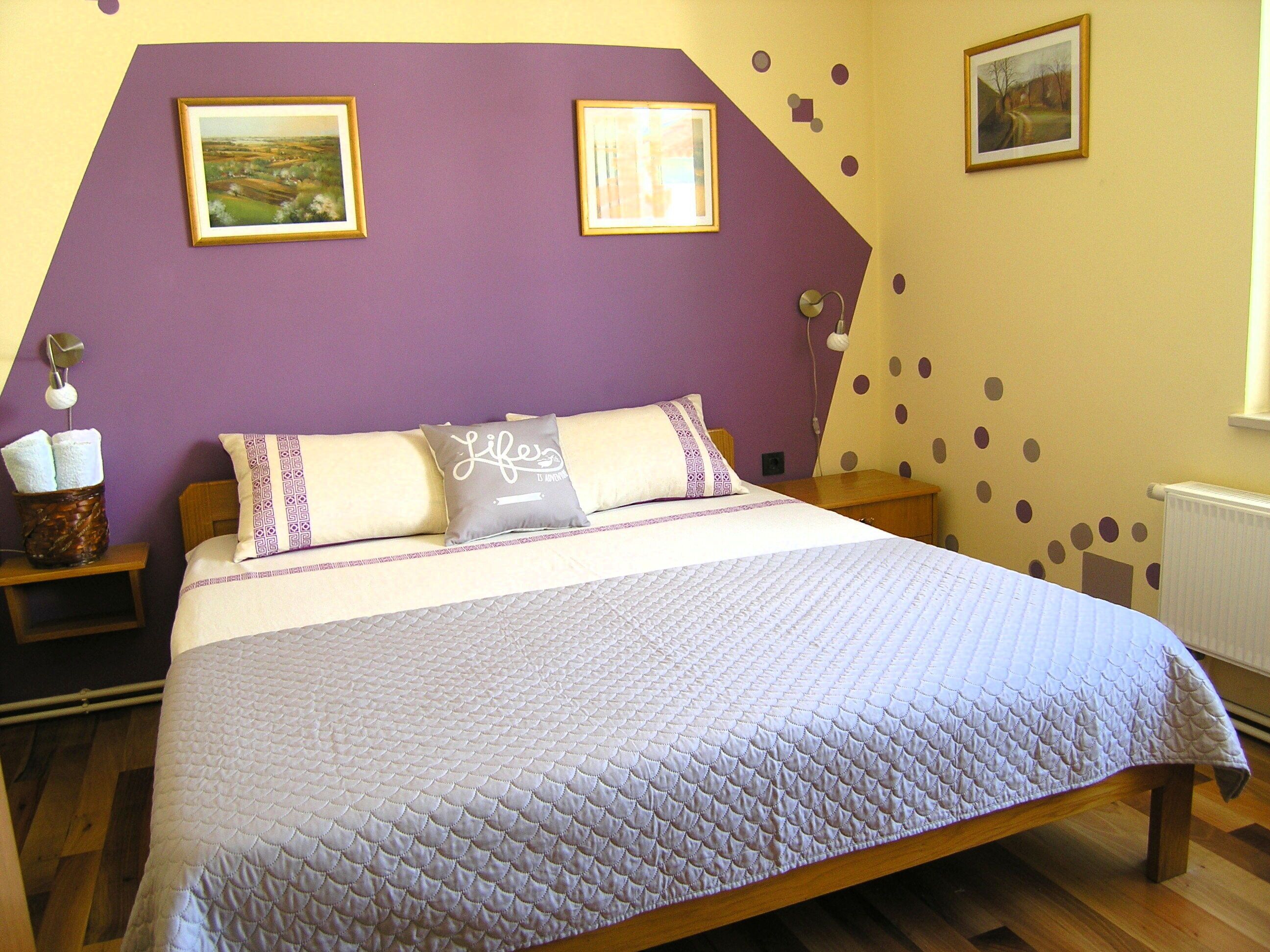 Een slaapkamer met een bed, twee kussens, een nachtkastje en een muur met foto's en decoratie.