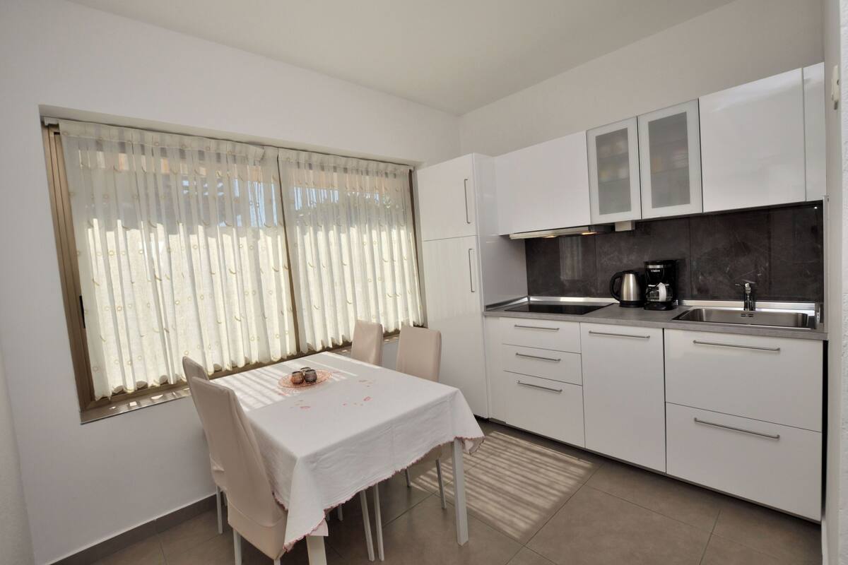 A modern kitchen with white cabinets, a stainless steel sink, and a window with sheer curtains.