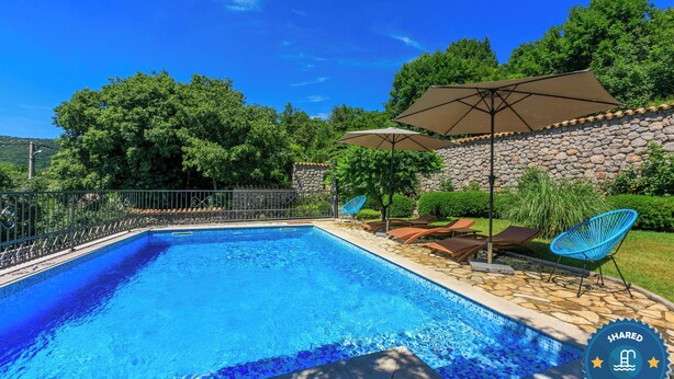 Una piscina con pared de piedra, sillas de descanso y sombrillas.