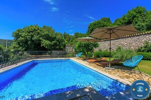 A swimming pool with a stone wall, lounge chairs, and umbrellas.