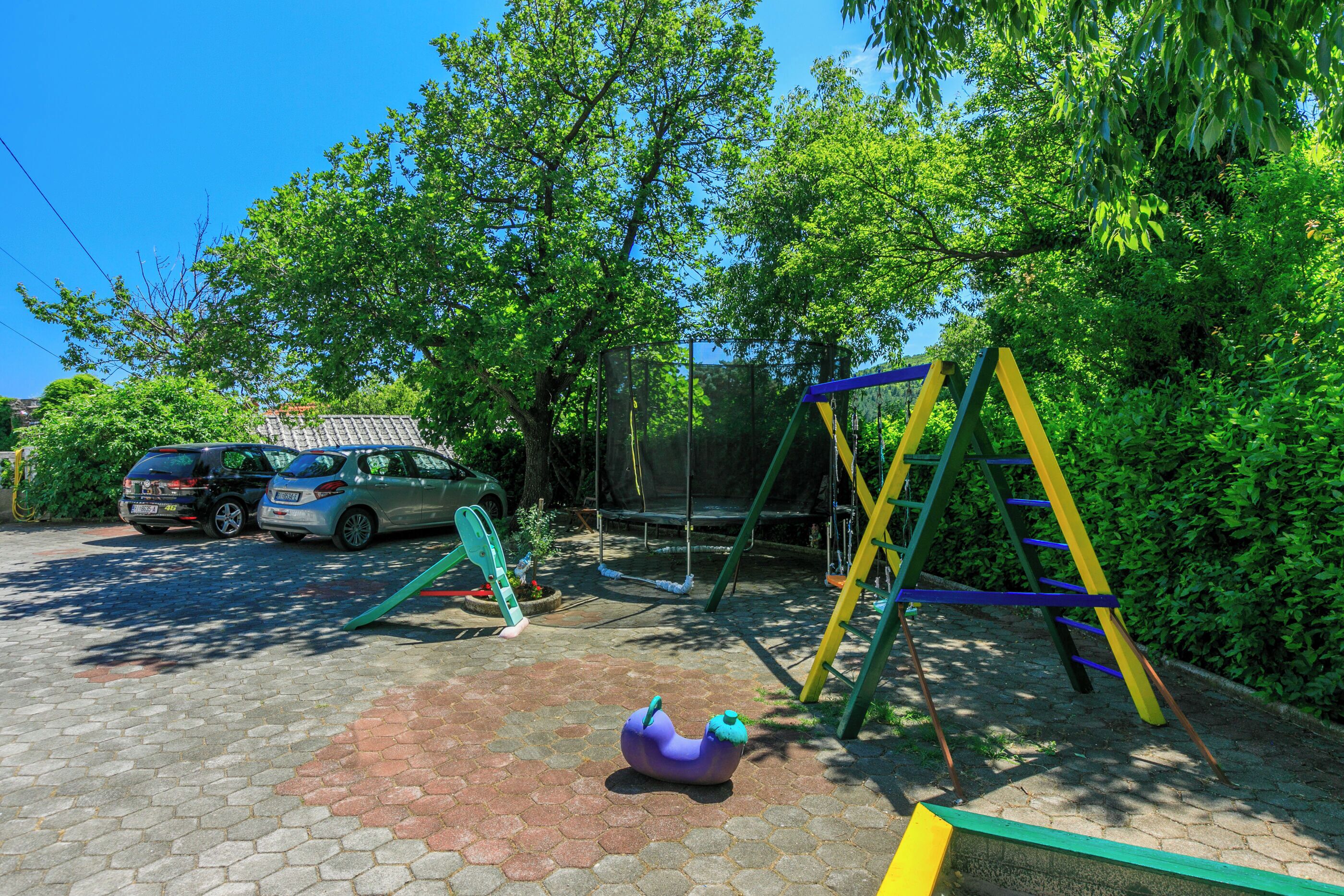 A playground with a swing set, a slide, and a purple spinning ride. There are two cars parked nearby.