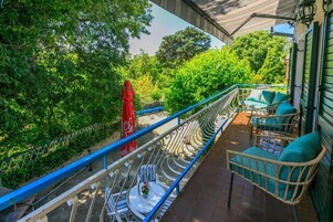 A balcony with wicker furniture, a red umbrella, and lush greenery in the background.