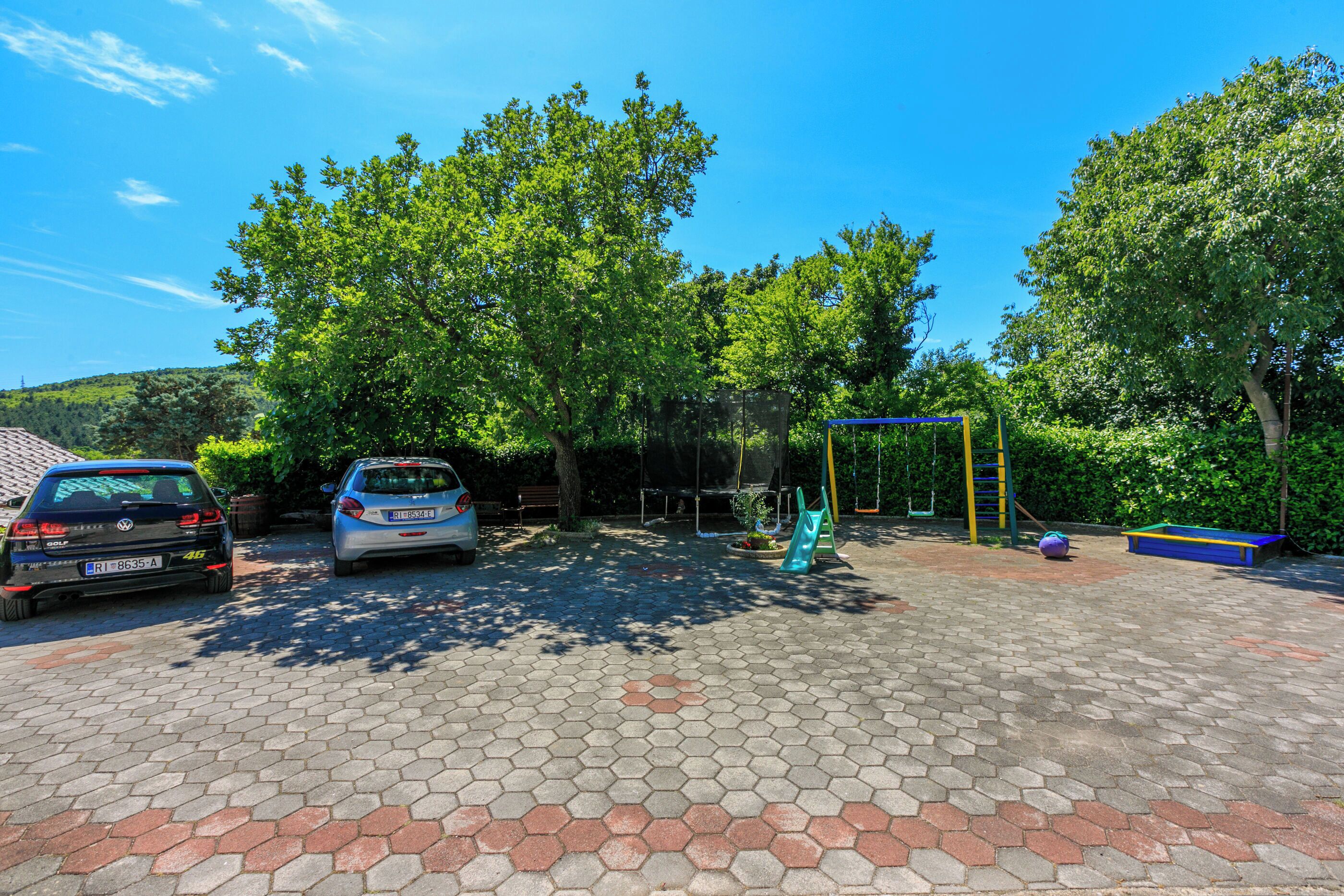 A parking area with hexagonal paving, two cars, and a playground with a swing set and slide.
