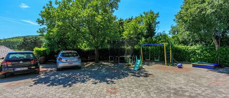 A parking area with hexagonal paving, two cars, and a playground with a swing set and slide.