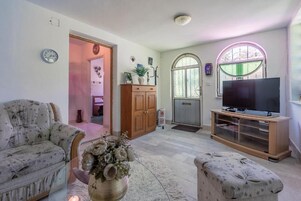 A living room with a sofa, ottoman, TV stand, and a decorative vase.