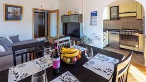 A dining area with a table set for two, a bottle of wine, and a bowl of fruit. - Apartments Anamarija (Novi Vinodolski)