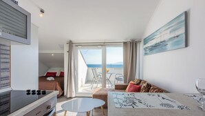 A modern hotel room with a kitchenette, a dining area, a sofa, and a balcony with a view of the sea. - Apartments Anamarija (Novi Vinodolski)