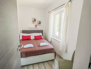 A bedroom with a bed, pillows, a window, and artwork on the wall. - Apartments Anamarija (Novi Vinodolski)