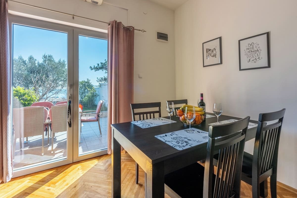 Un comedor con una mesa dispuesta para cuatro personas, dos marcos con citas inspiradoras en la pared y vistas a través de la puerta de cristal de un espacio exterior con asientos.