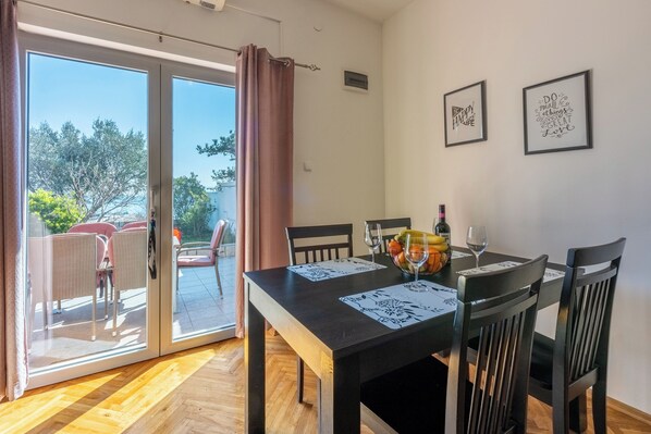 A dining area with a table set for four, two framed inspirational quotes on the wall, and a view through the glass door to an outdoor seating area. - Apartments Anamarija (Novi Vinodolski)