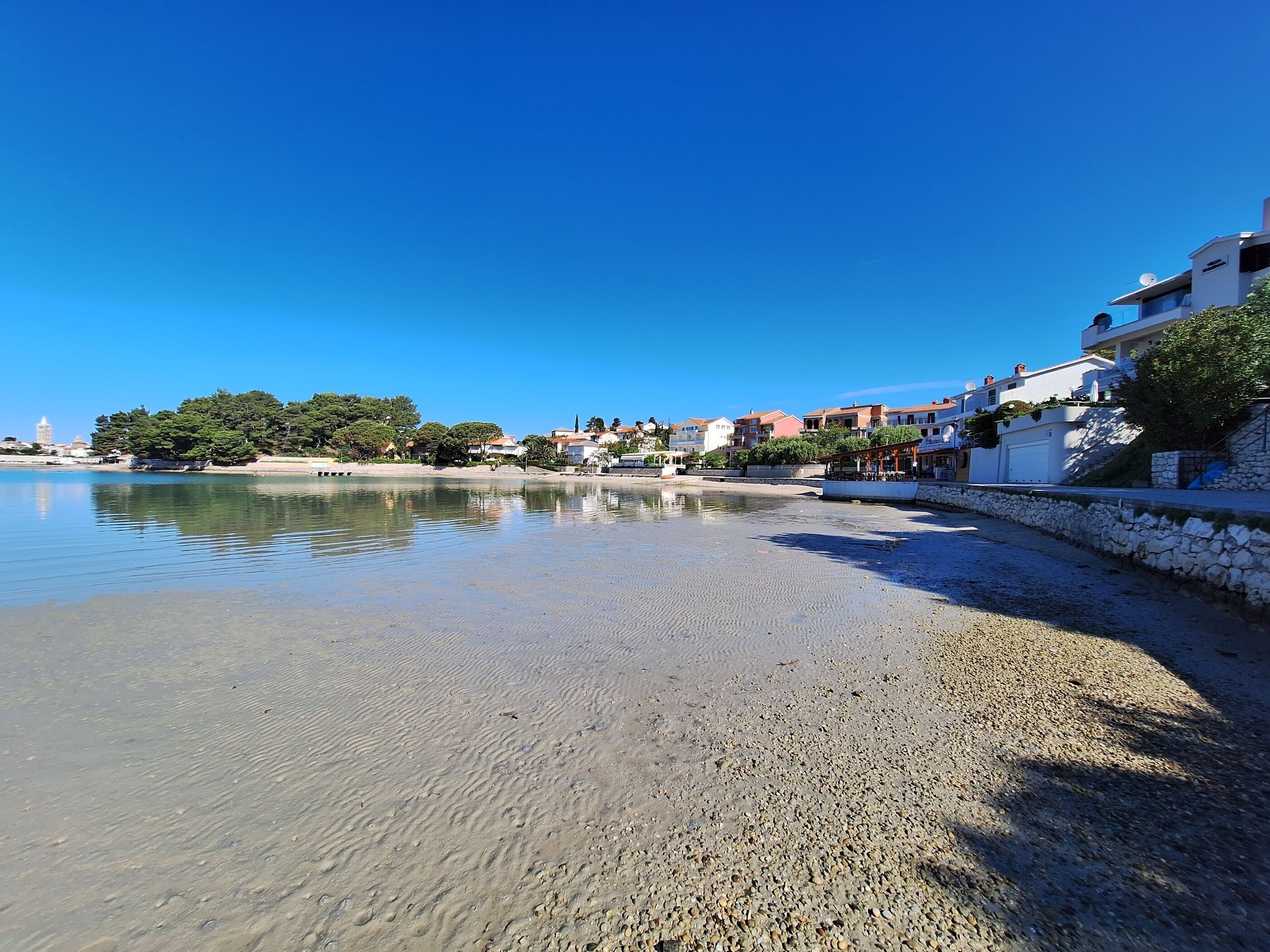 Una playa con agua cristalina, piedras y edificios a lo largo de la orilla.