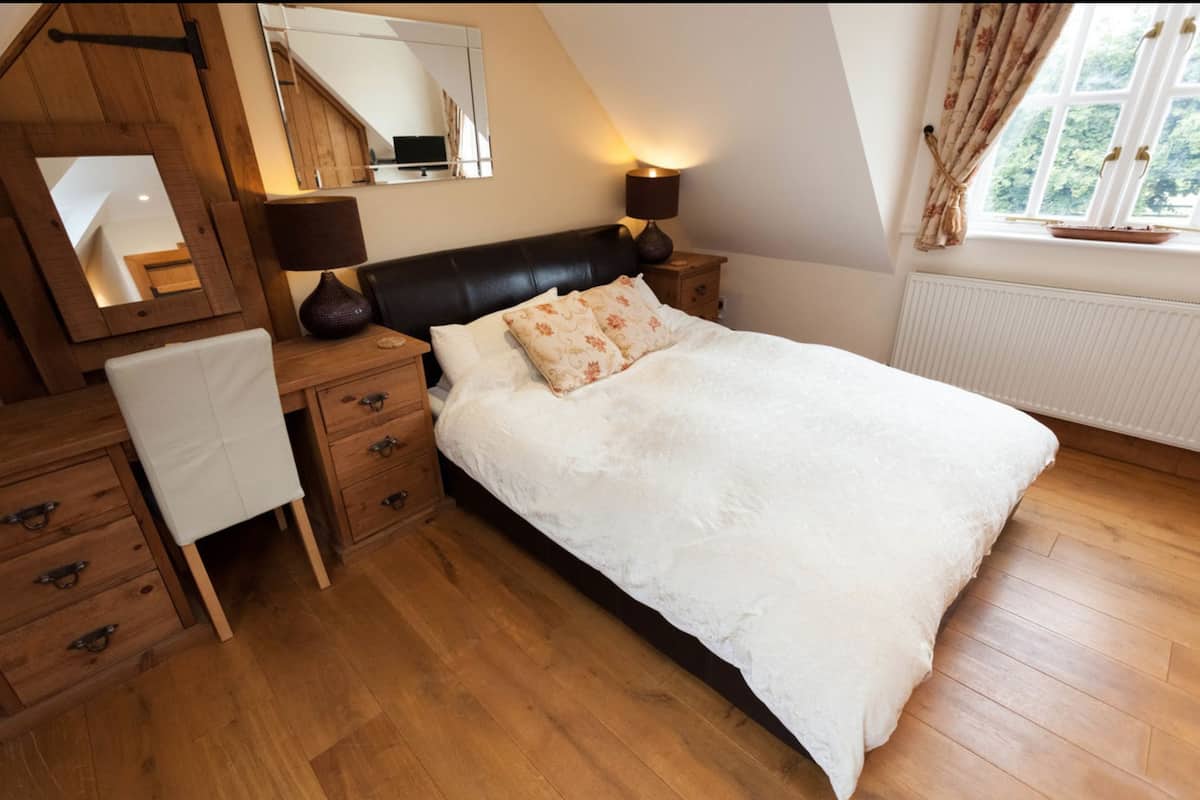A bedroom with a large bed, wooden furniture, a mirror, and a window with curtains.
