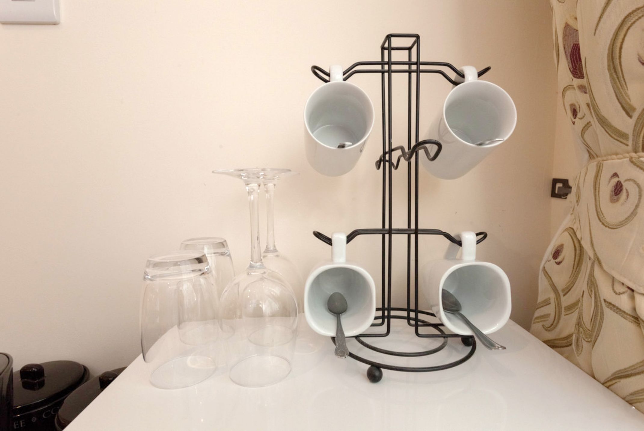 A white table with a black mug holder holding four white mugs and a wine glass.