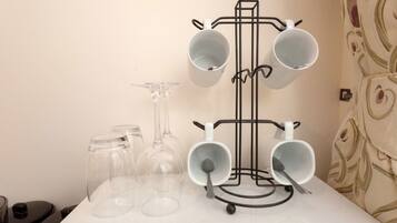 A white table with a black mug holder holding four white mugs and a wine glass.