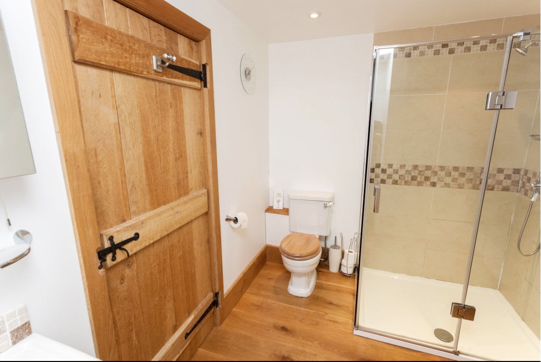 A bathroom with a wooden door, a toilet, a glass shower enclosure, and a tiled floor.