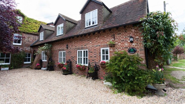 A traditional brick house with a gravel driveway, multiple windows, and hanging flower baskets. - Hanger Down House Bed and Breakfast (Arundel)