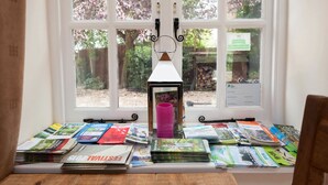 A room with a large window, a wooden table with magazines, and a pink candle holder. - Hanger Down House Bed and Breakfast (Arundel)